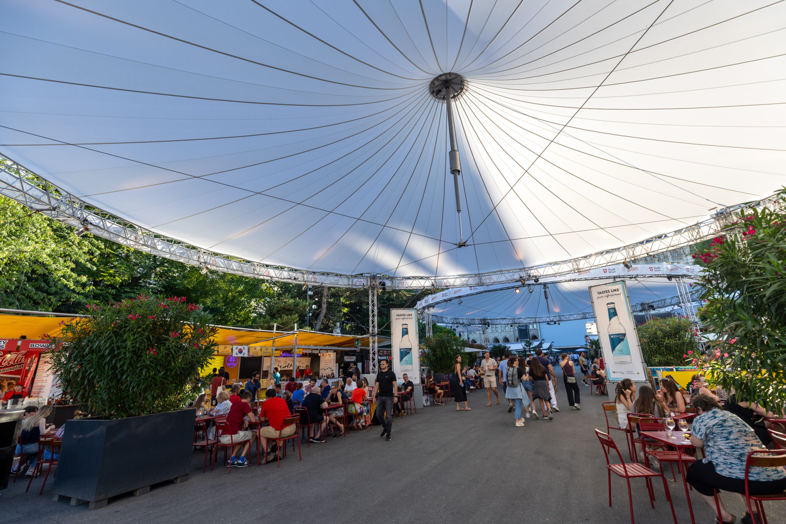 Übersicht der Gastronomiestände beim Film Festival unter einem großen Schirm. Personen sitzen an Tischen