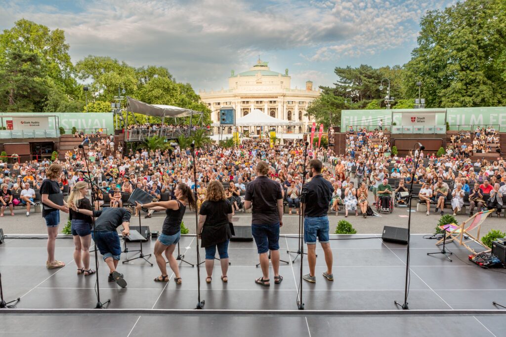 Menschen die auf der Bühne stehen vor einem Publikum am Rathausplatz.